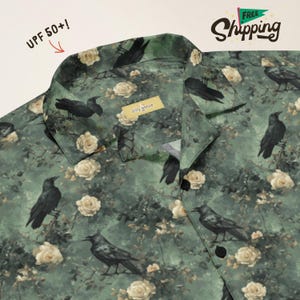 May include: A green button-down shirt featuring a repeating pattern of black crows and cream-colored roses. The collar area includes a small yellow tag with the text silly goose and a red arrow pointing to the text UPF 50+!.