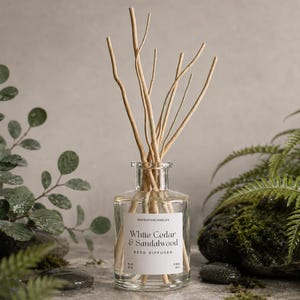 Könnte beinhalten: Ein Diffuser aus klarem Glas mit hellbraunen Holzstäbchen. Das weiße Etikett trägt die Aufschrift IndigoFoxCandles, White Cedar & Sandalwood, Reed Diffuser, No 02, 200 ml. Die Flasche hat einen kurzen Hals und einen breiten Boden.