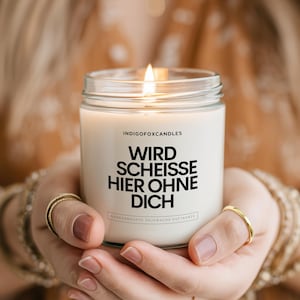 Könnte beinhalten: Eine Kerze im klaren Glasgefäß mit weißem Wachs und brennendem Docht. Das Etikett zeigt den schwarzen Schriftzug INDIGOFXRCANDLES gefolgt von WIRD SCHEISSE HIER OHNE DICH in fetten Großbuchstaben, mit kleinerem Text am unteren Rand des Etiketts.