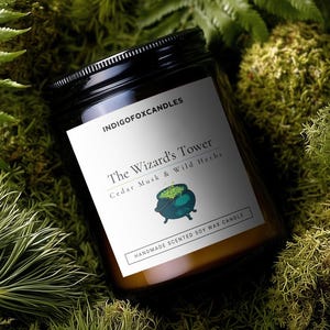 Op de afbeelding: Een glazen potkaars met een zwart deksel, met het opschrift "The Wizard's Tower" met de tekst "Cedar Musk & Wild Herbs" en een ketelafbeelding. De kaars staat op een bedje van groen mos en varens. Het etiket luidt ook "HANDMADE SCENTED SOY WAX CANDLE".