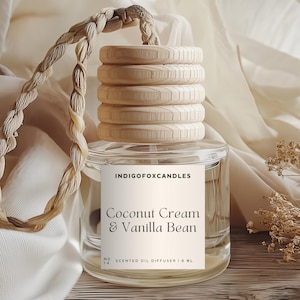 Könnte beinhalten: Ein klarer Glas-Duftöldiffusor mit einem Holzdeckel und einem geflochtenen Seil. Auf dem Etikett steht "Coconut Cream & Vanilla Bean". Der Diffusor wird auf einer Holzoberfläche mit einem weichen, weißen Stoff im Hintergrund präsentiert.