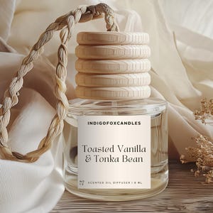 Könnte beinhalten: Ein klarer Glas-Duftöldiffusor mit einem Holzdeckel und einem geflochtenen Seil. Auf dem Etikett steht "Toasted Vanilla & Tonka Bean". Der Diffusor wird auf einer hellen Oberfläche mit neutralem Hintergrund präsentiert.