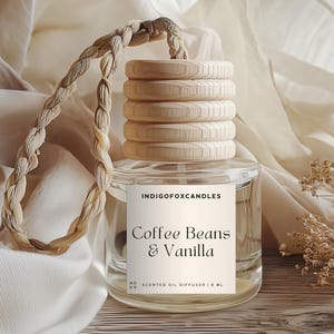 Könnte beinhalten: Ein klarer Glas-Duftöldiffusor mit einem Holzdeckel und einem geflochtenen Seilgriff. Auf dem Etikett steht "Coffee Beans & Vanilla". Der Diffusor wird auf einer Holzoberfläche mit einem weichen, neutralfarbenen Stoff im Hintergrund präsentiert.