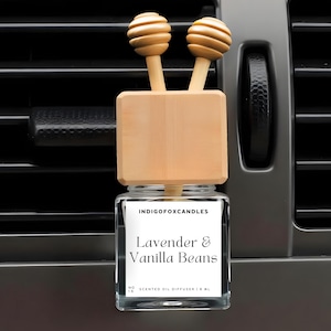 Könnte beinhalten: Ein Auto-Lufterfrischer mit einem Holzaufsatz und einem Glasbehälter. Auf dem Etikett steht "Lavender & Vanilla Beans". Der Lufterfrischer ist für die Platzierung in einer Lüftungsöffnung im Auto konzipiert. Der Holzaufsatz hat zwei dekorative Holzkugeln.