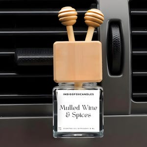 Könnte beinhalten: Ein Auto-Lufterfrischer mit einem Glasbehälter und Holzakzenten. Auf dem Etikett steht "Mulled Wine & Spices". Der Diffusor hat zwei Holzaufsätze und einen Holzblock. Der Lufterfrischer ist für die Platzierung in einer Autolüftung vorgesehen.