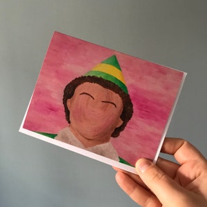 May include: A painting of a person wearing a green and yellow elf hat. The person's face is painted with a blank expression.