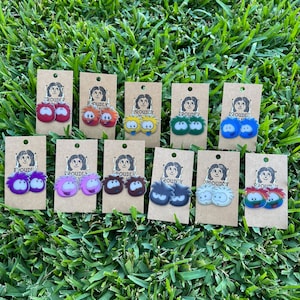 May include: A set of 10 pairs of earrings featuring cartoon characters with different colors and expressions. Each pair is displayed on a small card with the word "Proudly" printed on it.