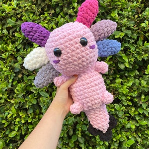 May include: A crocheted axolotl plush toy with a pink body and multi-colored fins. The fins are purple, white, gray, and pink.
