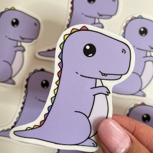 May include: A set of purple dinosaur stickers with rainbow spines. The dinosaurs have big eyes and are in a variety of poses.