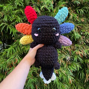May include: A black crocheted axolotl plush toy with rainbow colored crocheted gills. The axolotl has large black eyes and a white crocheted belly.
