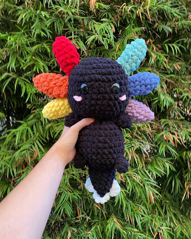 May include: A black crocheted axolotl plush toy with rainbow colored crocheted gills. The axolotl has large black eyes and a white crocheted belly.