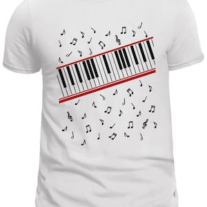 May include: White t-shirt featuring a piano keyboard design with black and white keys and a red border. Black musical notes are scattered around the keyboard graphic, creating a musical theme.