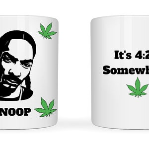 May include: White ceramic mug featuring a black silhouette of a celebrity's face, the name "SNOOP" in black, and green cannabis leaves. The other side of the mug has the text "It's 4:20 Somewhere" with a green cannabis leaf.