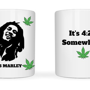 May include: White ceramic mug featuring a black silhouette of Bob Marley, surrounded by green cannabis leaves. The mug also displays the text "BOB MARLEY" and "It's 4:20 Somewhere" with a cannabis leaf graphic.