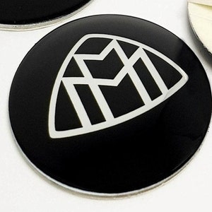 May include: A black and white emblem with a geometric design. The emblem is on a black round sticker.