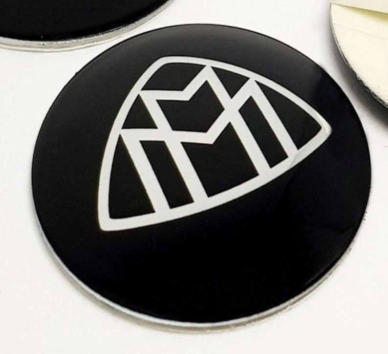 May include: A black and white emblem with a geometric design. The emblem is on a black round sticker.