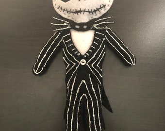 May include: A felt Jack Skellington doll with a black and white striped suit. The doll has a white face with black eyes and a stitched-on mouth.