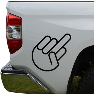 May include: Black outline of a hand with the middle finger extended, applied to the side of a white truck. The graphic is a bold, simple design, conveying a gesture of defiance or disapproval. The truck's taillight and bumper are visible.
