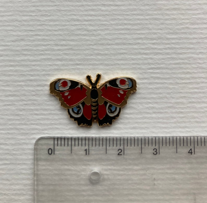May include: A gold-colored metal pin of a red, black, and blue butterfly with white spots. The butterfly is about 1.5 inches wide.
