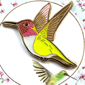 Könnte beinhalten: Eine goldfarbene Emaille-Anstecknadel mit einem Kolibri mit gelbem Körper, rosafarbenem und rotem Kopf und braunen Flügeln.