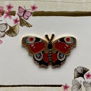 May include: A gold-tone butterfly pin with red, black, and blue accents. The butterfly has a detailed design and is a decorative piece.