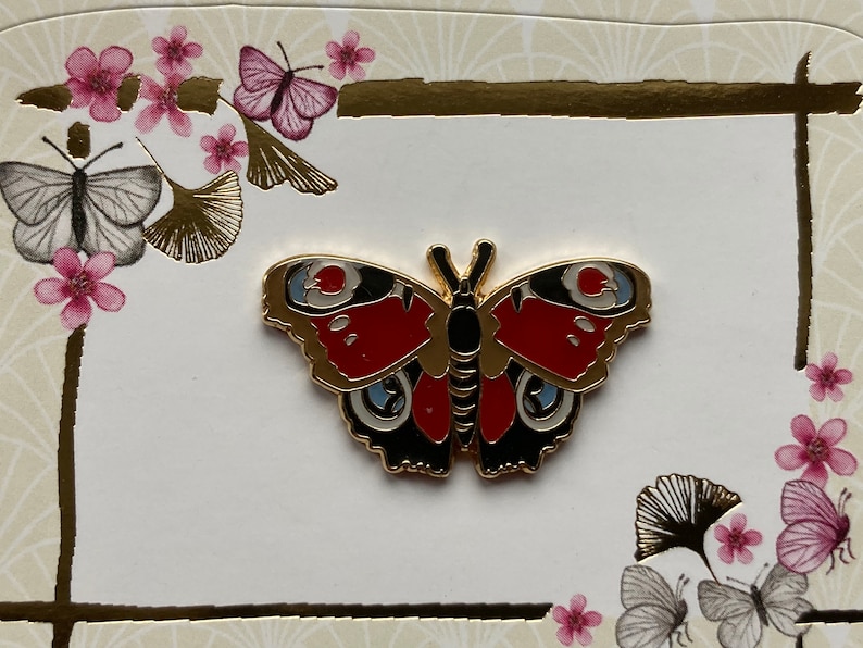 May include: A gold-tone butterfly pin with red, black, and blue accents. The butterfly has a detailed design and is a decorative piece.