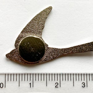 K&ouml;nnte beinhalten: Eine goldfarbene Metall-Vogelstecknadel mit magnetischer R&uuml;ckseite. Die Stecknadel ist etwa 5 cm lang und hat die Form eines Vogels im Flug.