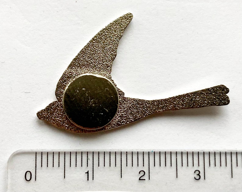 K&ouml;nnte beinhalten: Eine goldfarbene Metall-Vogelstecknadel mit magnetischer R&uuml;ckseite. Die Stecknadel ist etwa 5 cm lang und hat die Form eines Vogels im Flug.