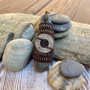 May include: A brown leather cord necklace with a round silver token that reads "One Was Not Enough" and "For Trade" with a brown stone pendant.
