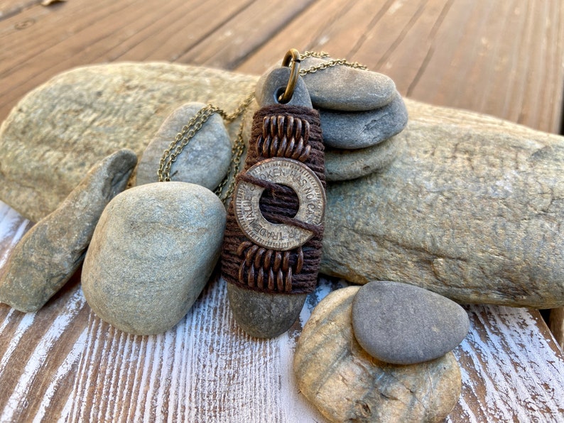 May include: A brown leather cord necklace with a round silver token that reads "One Was Not Enough" and "For Trade" with a brown stone pendant.