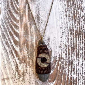 May include: A brown stone pendant necklace with a brass coin wrapped in brown leather cord. The coin has the words "Trade Token" inscribed on it.