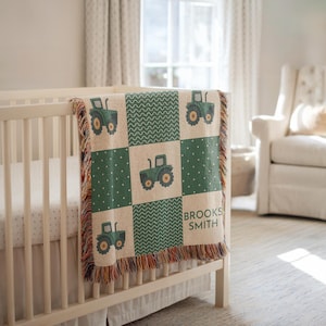 May include: A green and beige baby blanket with a tractor design. The blanket is square and features a patchwork pattern with green squares, white polka dots, and a wavy design. The name "BROOKS SMITH" is printed on the blanket.