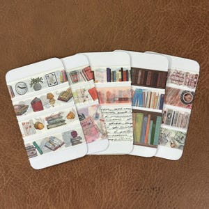 May include: Five rectangular cards displaying various rolls of decorative adhesive tape. The designs feature illustrations of books, bookshelves, clocks, plants, coffee cups, handwritten script, and autumn leaves in muted tones of brown, red, blue, and green.