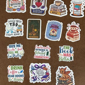 Peut inclure: Une collection d'autocollants colorés sur le thème des livres. Les autocollants présentent des phrases telles que "Cozy Bookish Weekend", "Fantasy Reads are my Jam" et "Drink Coffee Read Books Be Happy". D'autres autocollants représentent des livres, des tasses à café et un dragon.