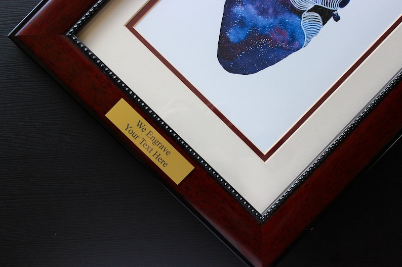 K&ouml;nnte beinhalten: Nahaufnahme eines gerahmten Drucks eines galaxief&ouml;rmigen Herzens. Der Rahmen ist aus dunklem Holz mit einer goldfarbenen Plakette, auf der "We Engrave Your Text Here" steht.