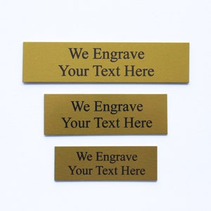 K&ouml;nnte beinhalten: Drei goldfarbene Metallplaketten mit dem Text "We Engrave Your Text Here" auf jeder.