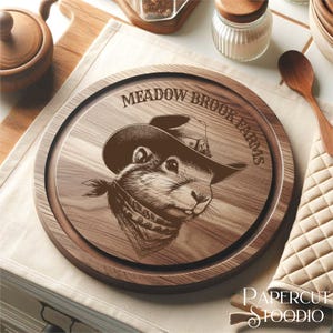 May include: A round wooden cutting board with a brown wood grain finish. The board has a decorative design of a prairie dog wearing a cowboy hat and bandana. The text "Meadow Brook Farms" is engraved around the edge of the board.