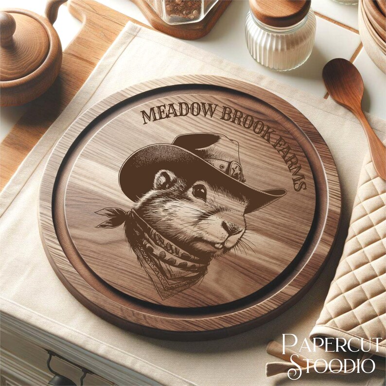 May include: A round wooden cutting board with a brown wood grain finish. The board has a decorative design of a prairie dog wearing a cowboy hat and bandana. The text "Meadow Brook Farms" is engraved around the edge of the board.