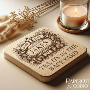 Puede incluir: Un posavasos de madera con un dise&ntilde;o grabado con l&aacute;ser que presenta un logotipo de pub con el texto "Jakes Pub" y las palabras "Good Time, Good Food, Great Beer". El posavasos tambi&eacute;n tiene el texto "Yes, it's in the backyard".