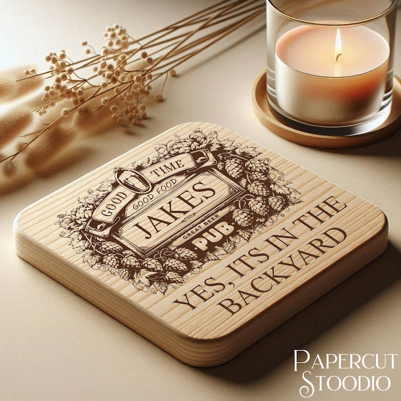 Puede incluir: Un posavasos de madera con un dise&ntilde;o grabado con l&aacute;ser que presenta un logotipo de pub con el texto "Jakes Pub" y las palabras "Good Time, Good Food, Great Beer". El posavasos tambi&eacute;n tiene el texto "Yes, it's in the backyard".