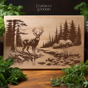 Puede incluir: Tabla de cortar de madera con una imagen grabada de un ciervo en un bosque. El ciervo está cerca de un arroyo con árboles al fondo. El texto "PAPERCUT STOODIO" está en la parte superior.