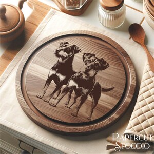Może przedstawiać: Okrągła drewniana deska do serwowania z ciemnobrązową obw&oacute;dką i jaśniejszym środkiem z usłojeniem drewna. Środek przedstawia wytrawiony obraz dw&oacute;ch ps&oacute;w. Słowa "PAPERCUT STOODIO" są wydrukowane w prawym dolnym rogu.