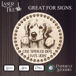 Może przedstawiać: Okrągły drewniany znak z szczeg&oacute;łowym grawerunkiem psa Golden Retrievera wyglądającego zza płotu. Znak jest obramowany odciskami łap i zawiera napis "One spoiled dog lives here". Znak jest oznaczony "Great for Signs".