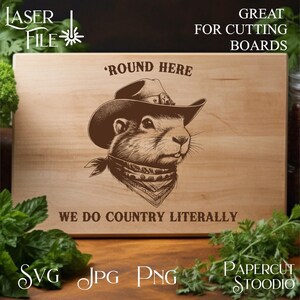 May include: A wooden cutting board with a brown illustration of a prairie dog wearing a cowboy hat and bandana. The text "Round Here" and "We Do Country Literally" is printed on the board.