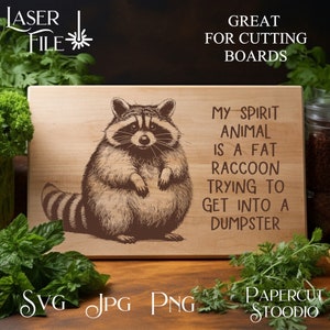 May include: A wooden cutting board with a black and white illustration of a raccoon. The text on the board reads "My spirit animal is a fat raccoon trying to get into a dumpster."