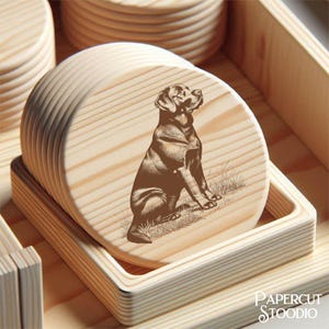 May include: A set of round wooden coasters with a laser-etched image of a Labrador Retriever dog. The coasters are light brown and are stacked in a square wooden holder. The image is a detailed illustration of the dog.