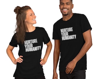 May include: Black t-shirts with the text "NURTURE YOUR HUMANITY" in white. The shirts are short-sleeved and worn by two people. The image is a medium shot, showing the shirts and the people wearing them.