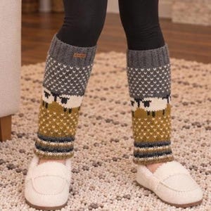 May include: A cream-colored long-sleeve knit sweater, black leggings, and patterned leg warmers featuring a sheep motif in shades of gray, mustard yellow, and white, paired with white slip-on shoes. The leg warmers have a ribbed cuff at the top.