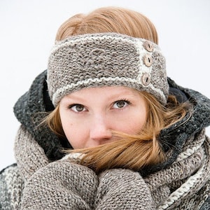 May include: A woman wearing a brown knitted headband with white trim and wooden buttons. The headband is covering her ears. She is also wearing a brown knitted scarf and sweater.