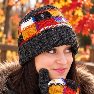 May include: A charcoal gray knit beanie and matching mitten featuring a colorful patchwork design of red, orange, yellow, and white squares. The beanie has a thick ribbed cuff, and both items are accented with decorative white and red cross-stitching.